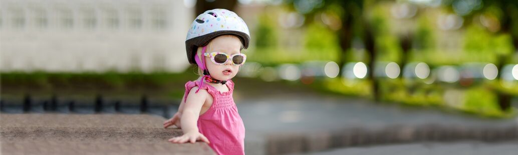 Kind mit Fahrradhelm und Sonnenbrille lehnt entspannt gegen eine halbhohe Steinmauer