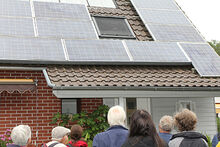 Menschen stehen vor einem Haus, auf dessen Dach eine Photovoltaikanlage installiert ist